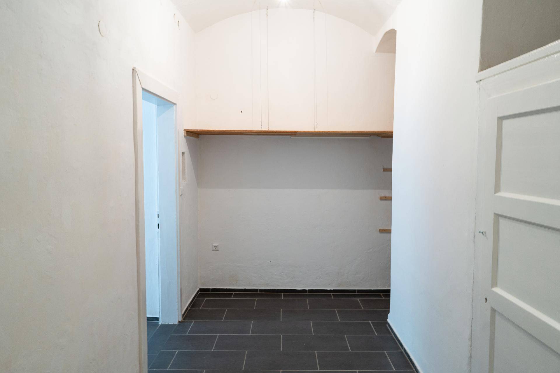Praktischer Abstellraum mit gewölbter Decke, Regalen und dunklem Fliesenboden.