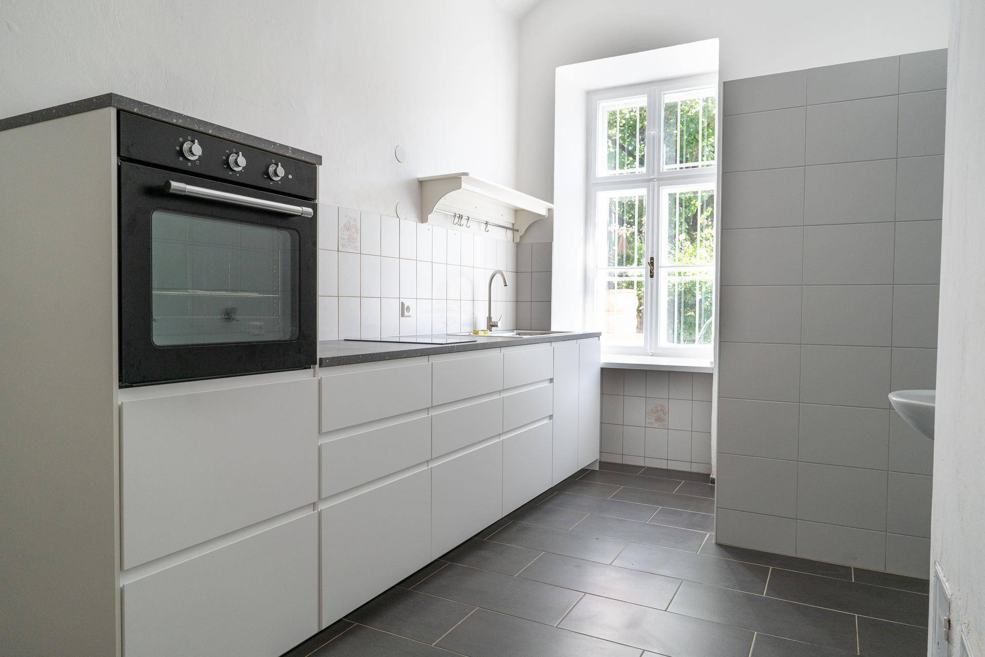 Funktionale Küche mit weißen Unterschränken, Backofen und Fenster mit Blick ins Grüne.