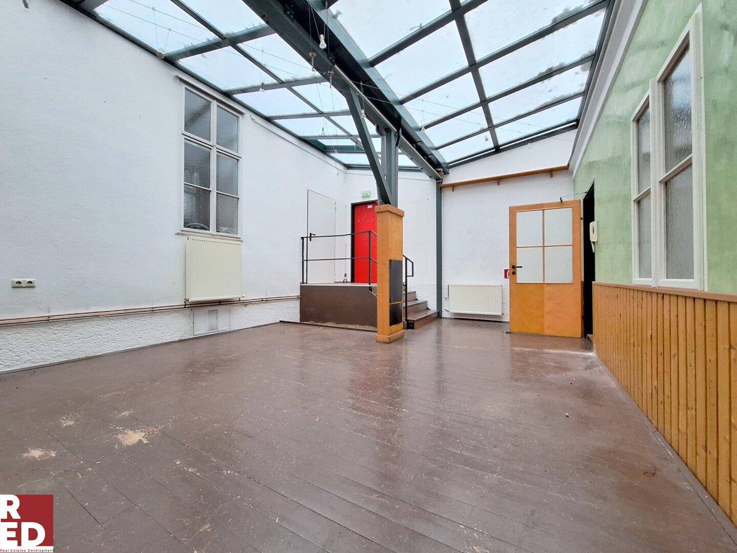 Geräumiger, leerer Workshop-Raum mit Glasdach, Holzboden und hohen Wänden.