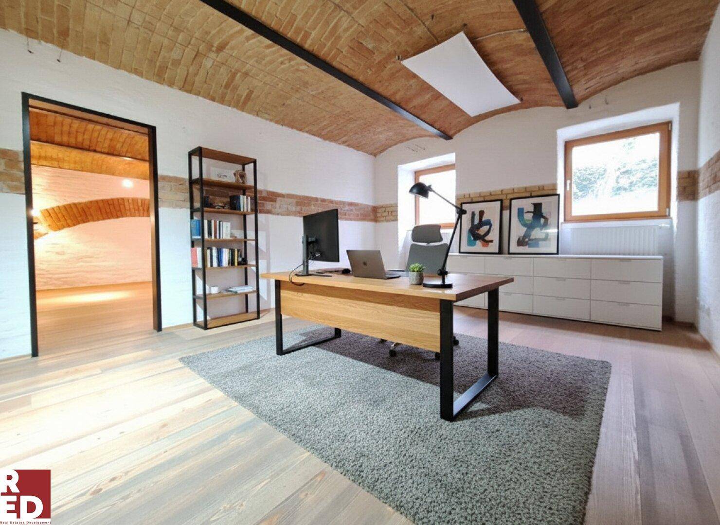 Modernes Büro mit Holzboden, Ziegelgewölbedecke und einem Schreibtisch mit Computer.