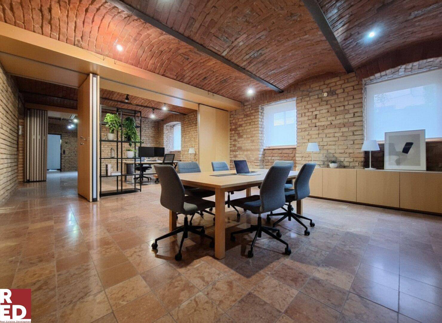 Geräumiges Büro mit gefliestem Boden, Besprechungstisch und Schiebetüren zu weiteren Arbeitsbereichen.