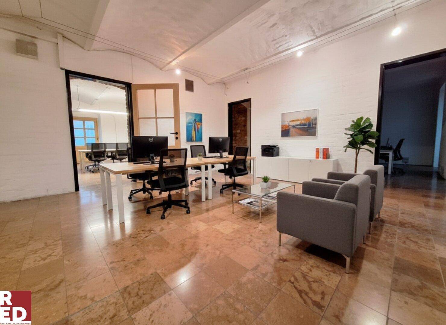 Modernes Büro mit gefliestem Boden, mehreren Arbeitsplätzen und einer gemütlichen Sitzecke.