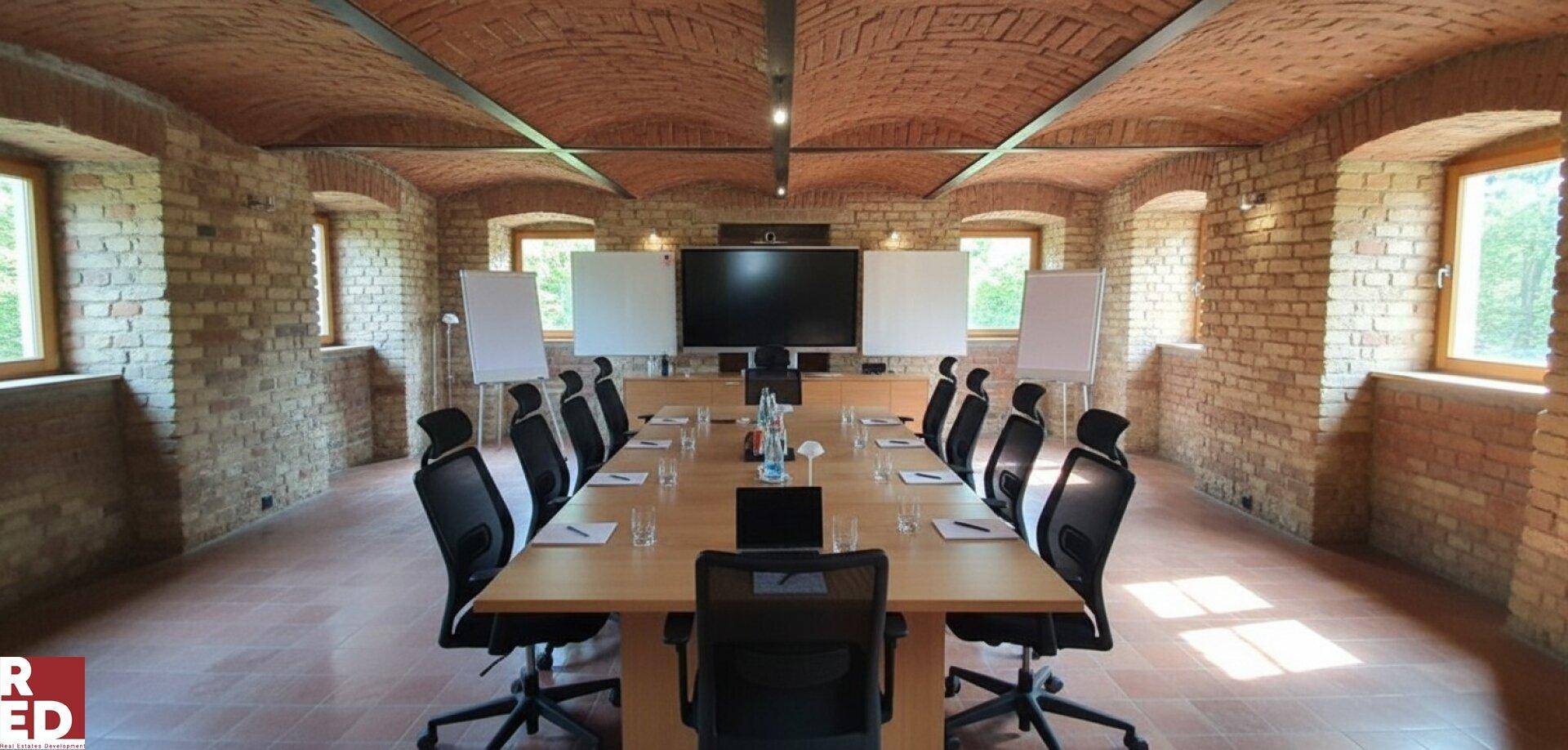Großer Konferenzraum mit Ziegelgewölbedecke, Holztisch und Präsentationsbildschirm.