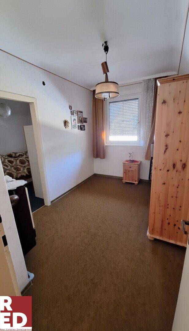 Kleines Schlafzimmer mit Teppichboden, einem Fenster und einem rustikalen Holzschrank.