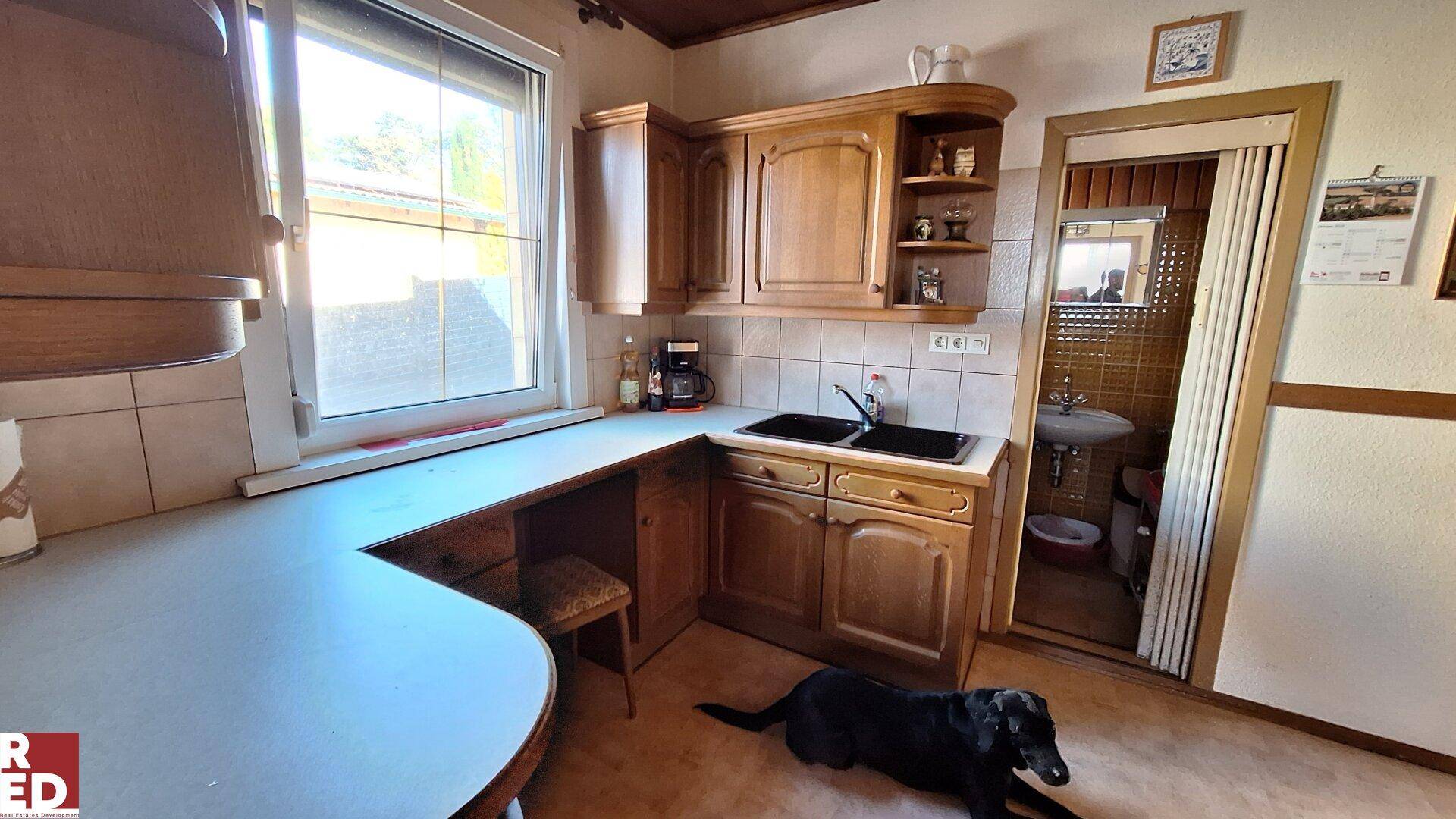 Traditionelle Holzküche mit Fliesenboden, Spülbecken und Blick in ein kleines Badezimmer.