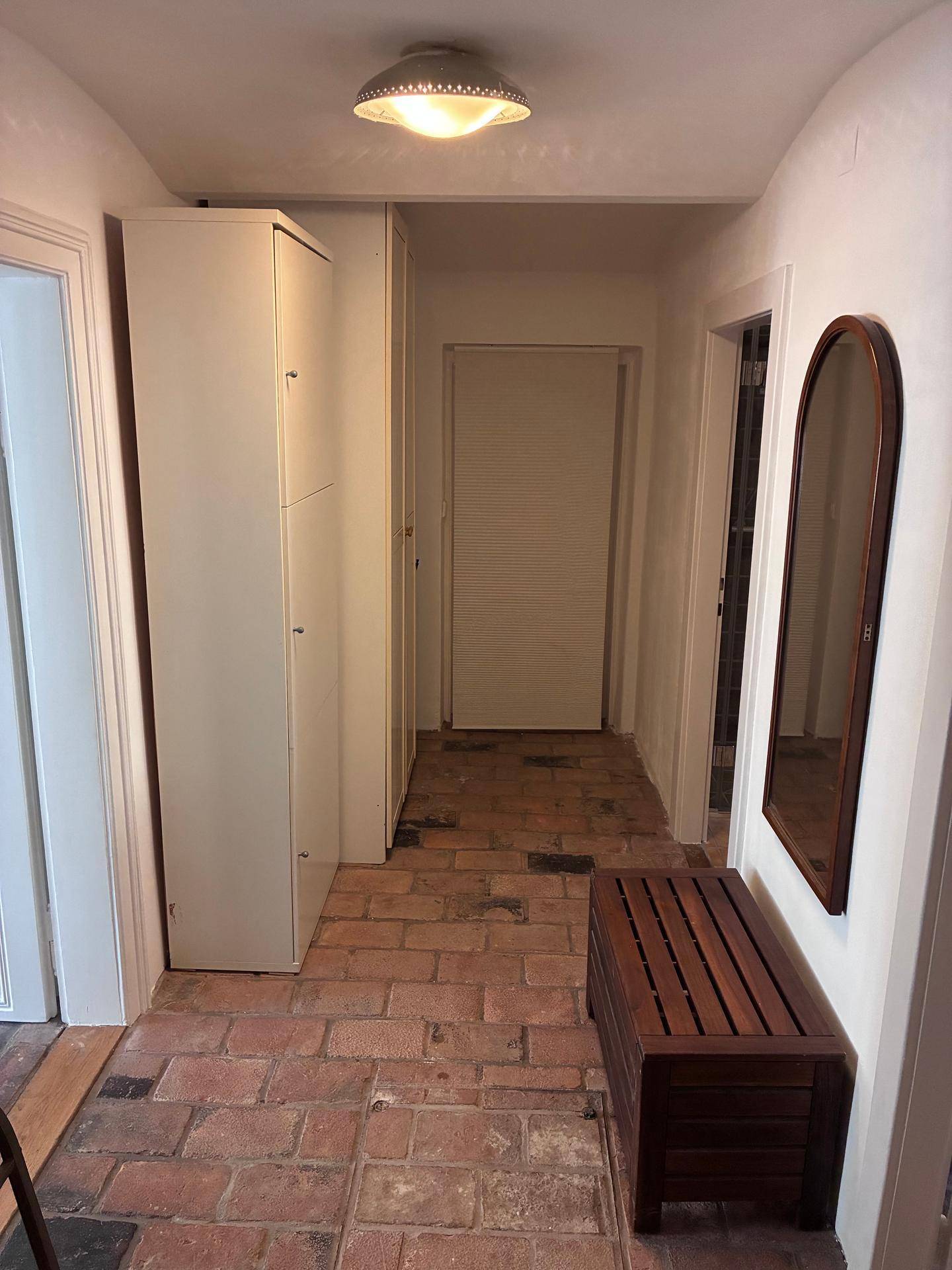 Langer Flur mit Ziegelboden, Einbauschrank und Spiegel.