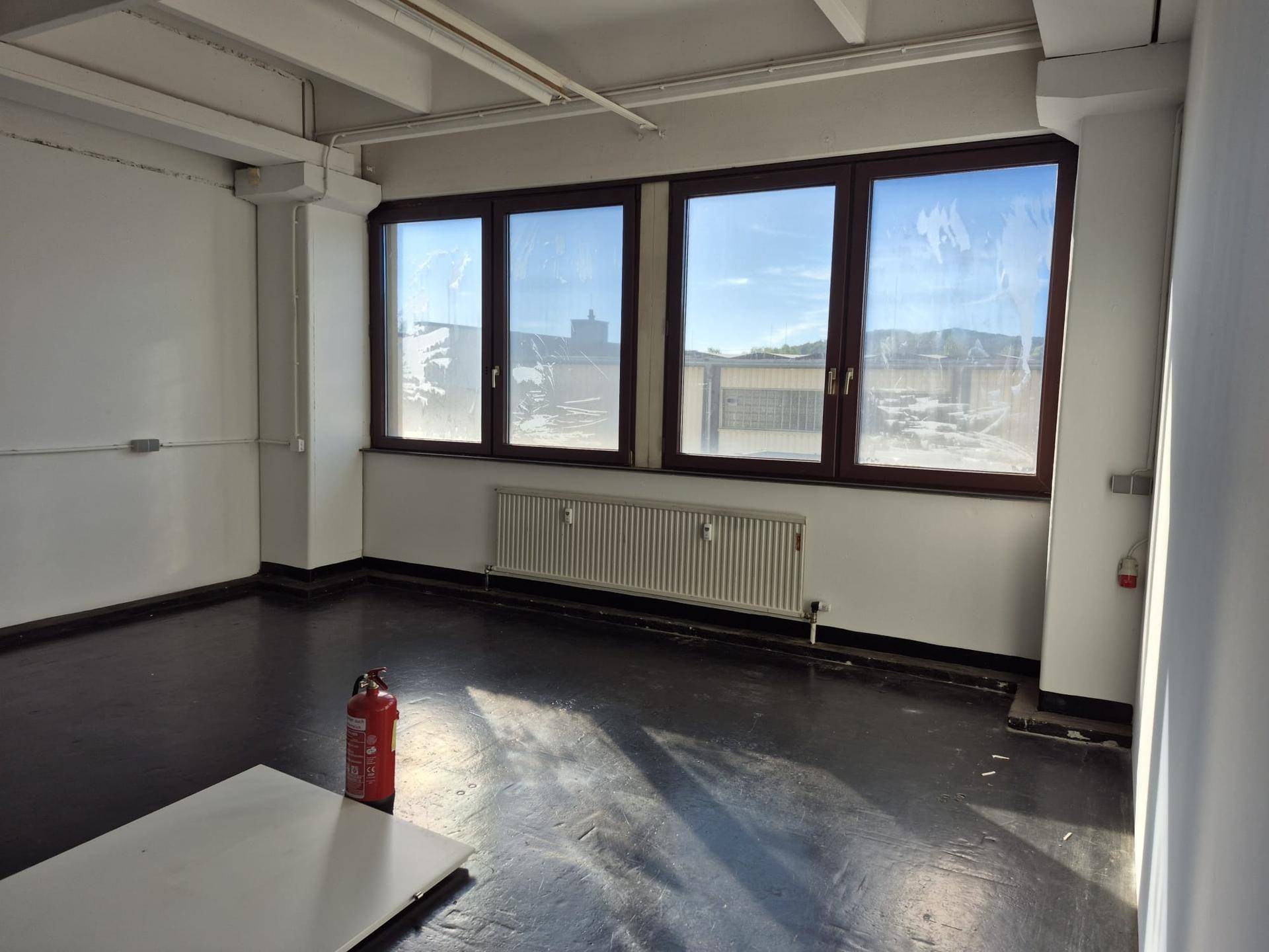 Heller Lagerraum mit dunklem Betonboden, hohen Decken und großen Fenstern für viel Licht.
