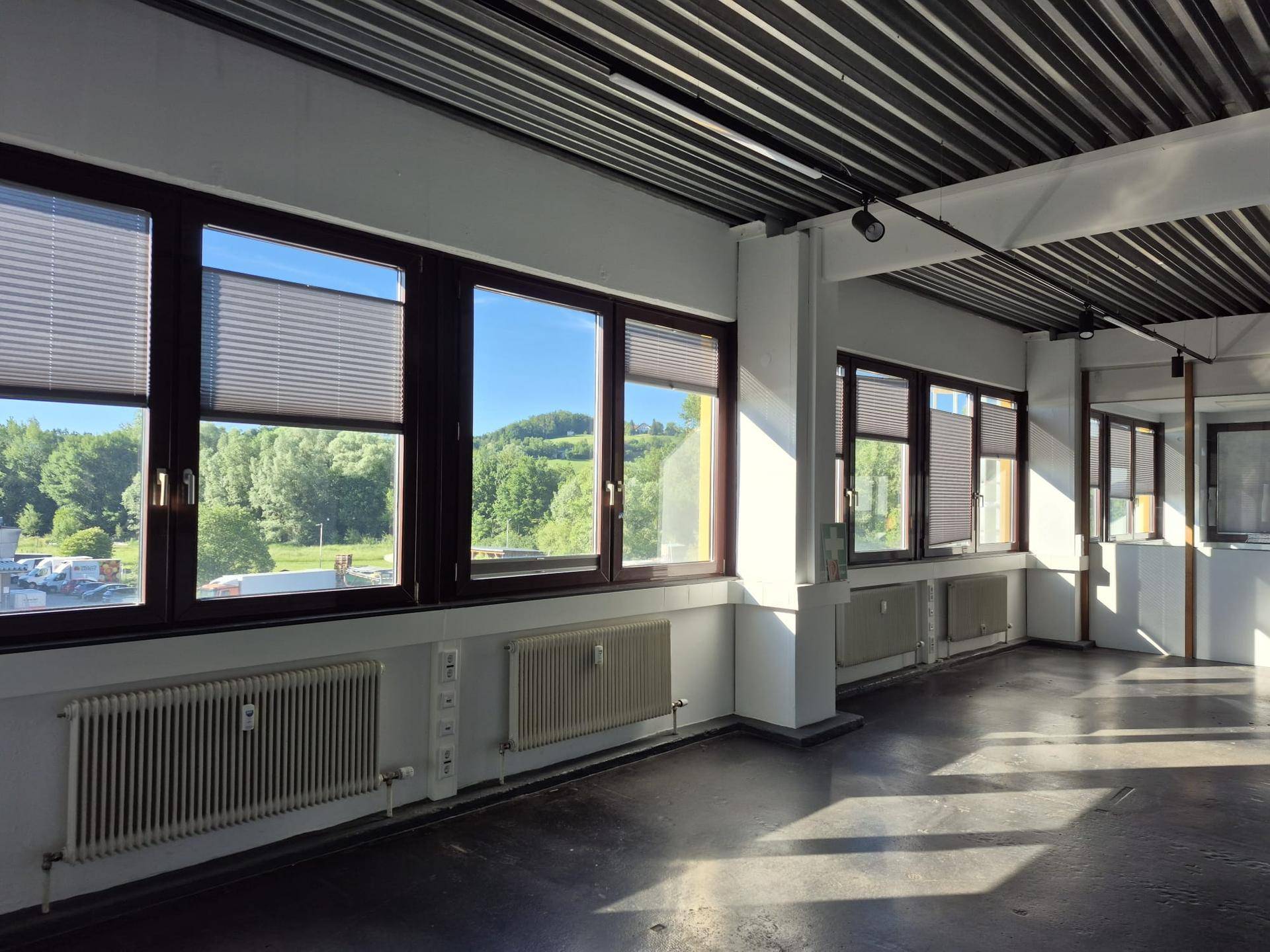 Weitläufiger Bürobereich mit Betonboden und einer Fensterfront, die viel Tageslicht und einen weiten Blick bietet.