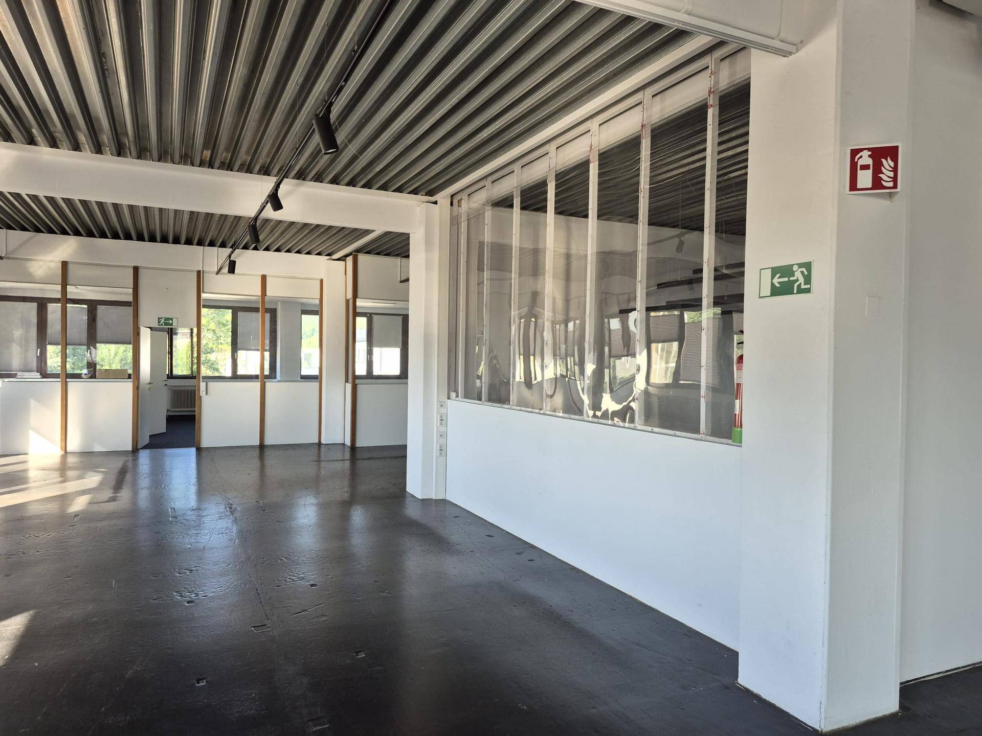 Offener Bürobereich mit Betonboden, flexiblen Glaswänden und sichtbaren Deckeninstallationen, ideal für moderne Arbeitskonzepte.