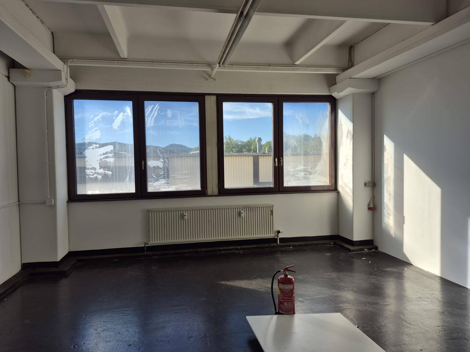 Geräumiger Lagerraum mit dunklem Betonboden, hohen Decken und weitem Ausblick durch die Fenster.