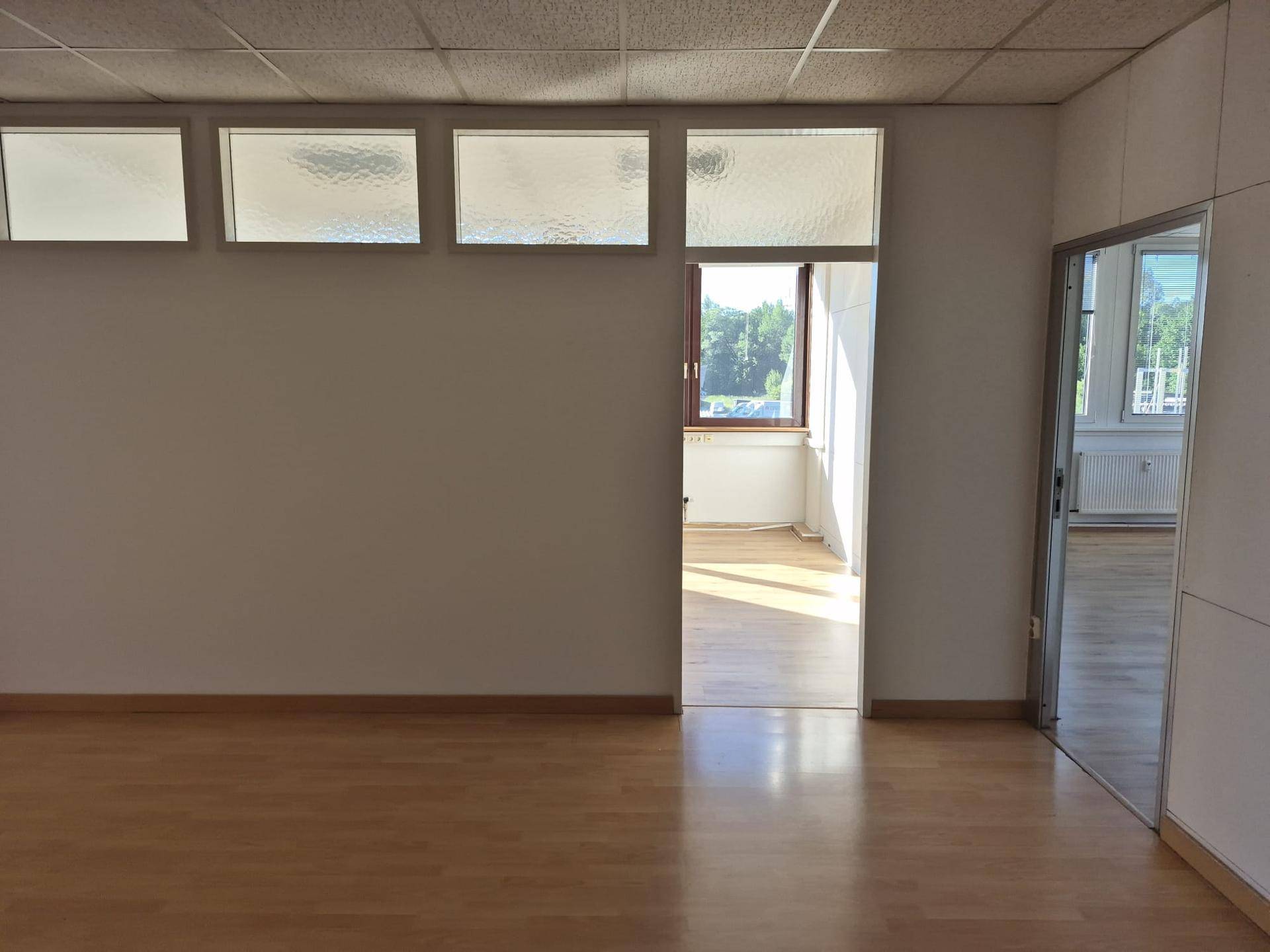Geräumiges Büro mit Laminatboden, hellen Wänden und viel Tageslicht durch die Fenster.