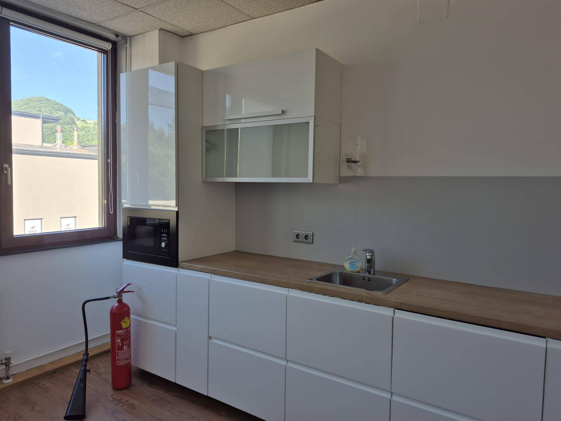 Moderne Küchenzeile mit weißen Hochglanzschränken, Holzplatte und integrierter Mikrowelle.