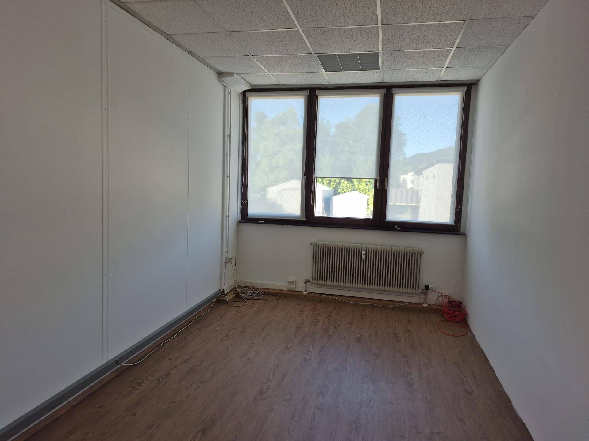 Kleiner Büroraum mit Laminatboden, Fenster mit Jalousien und einem Heizkörper an der Wand.