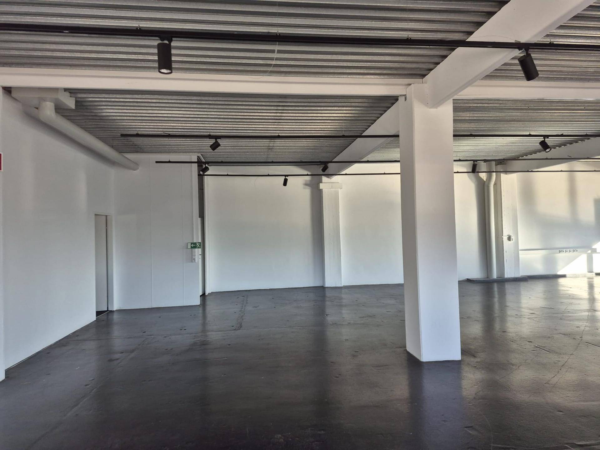 Großer, offener Büroraum mit Betonboden, weißen Wänden und sichtbaren Deckeninstallationen, bereit zur Gestaltung.