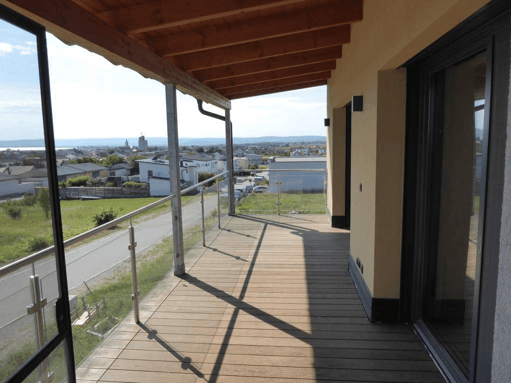 Geräumiger Balkon mit Holzboden, Glasgeländer und weitem Blick über die Umgebung.