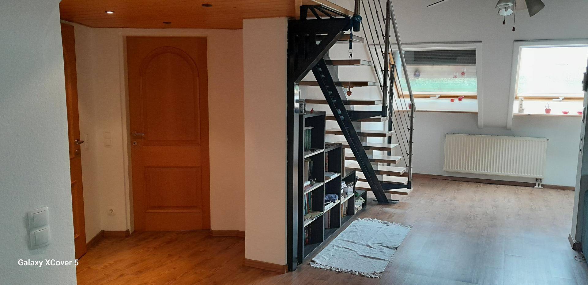 Heller Flur mit Holzfußboden, Holztür und moderner Wendeltreppe mit integriertem Regal.