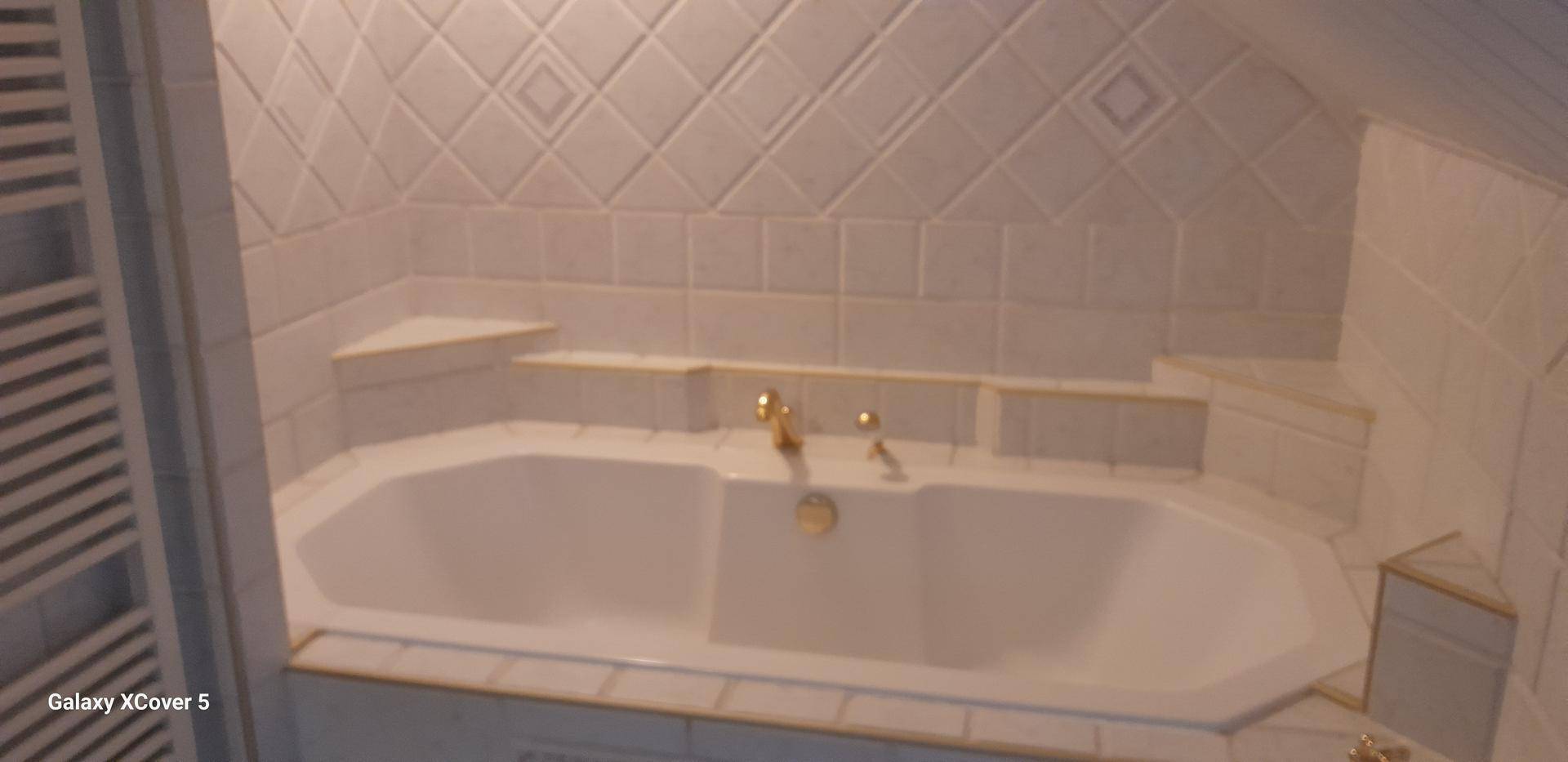 Badezimmer mit Eckbadewanne, gefliesten Wänden und beheiztem Handtuchhalter unter Dachschräge.