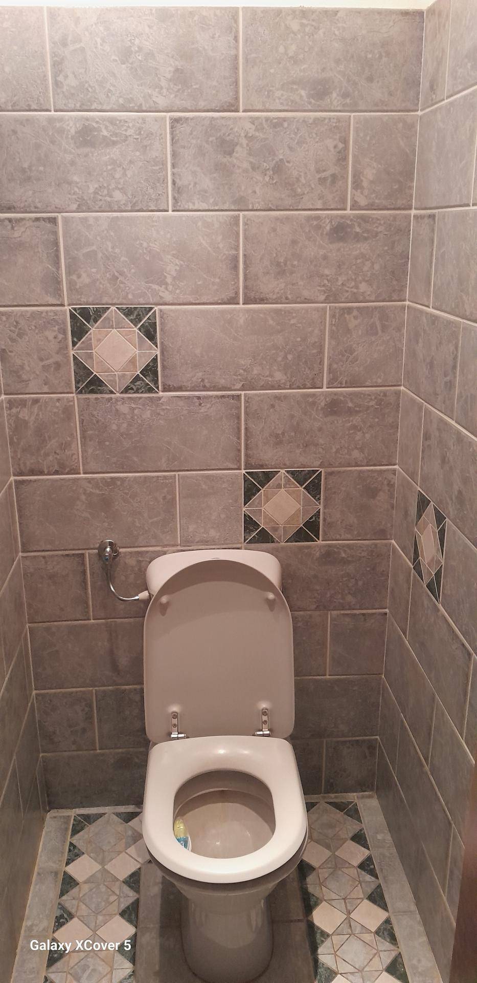 Kleines WC mit grauen Fliesen an Wänden und Boden, inklusive dekorativer Muster.