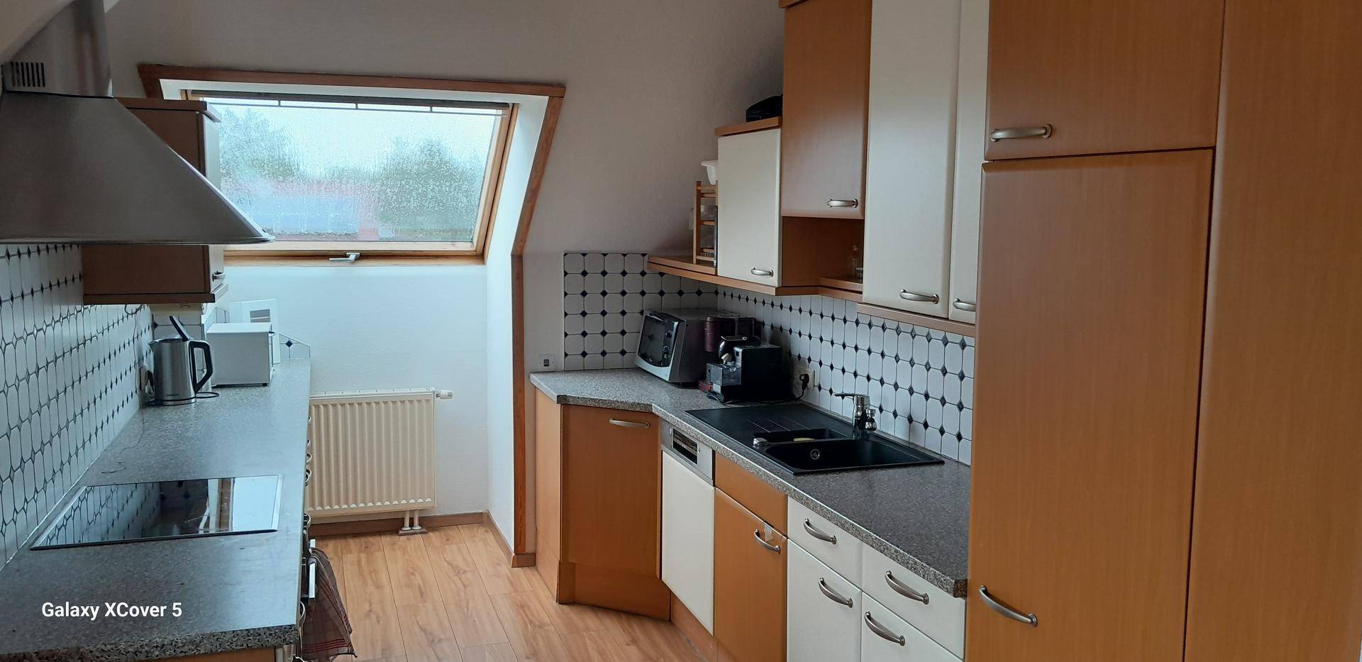 Funktionale Küche mit Holzschränken, dunkler Arbeitsplatte und Dachfenster, gut ausgestattet.