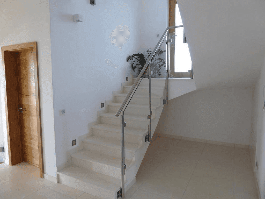 Elegante Treppe mit Fliesenstufen, Glasgeländer und indirekter Beleuchtung im Flurbereich.