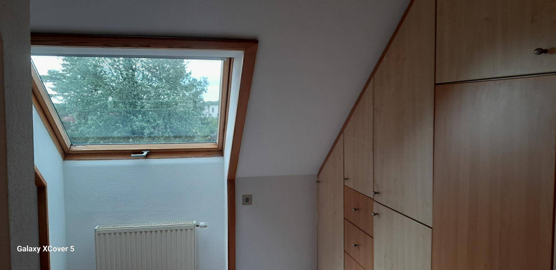 Schlafzimmer im Dachgeschoss mit Dachfenster, Heizkörper und integrierten Holzschränken.
