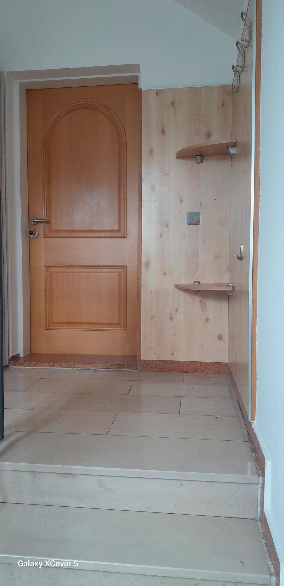 Heller Eingangsbereich mit Holztür, gefliestem Boden und praktischer Garderobenlösung.