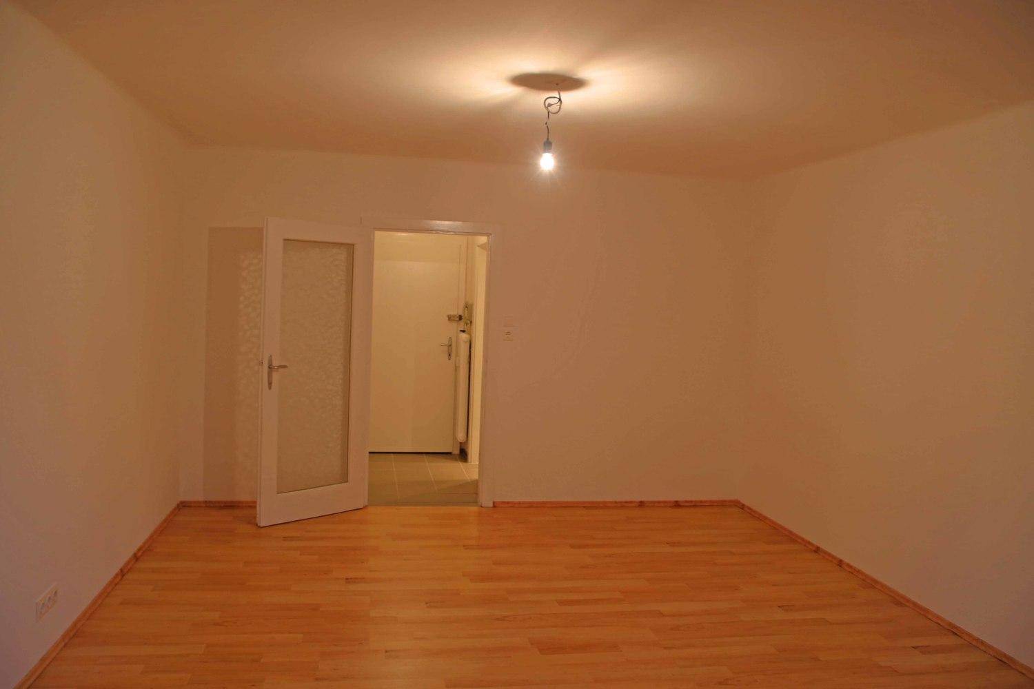Leeres Zimmer mit Parkettboden und einer Tür, die in einen weiteren Raum führt.