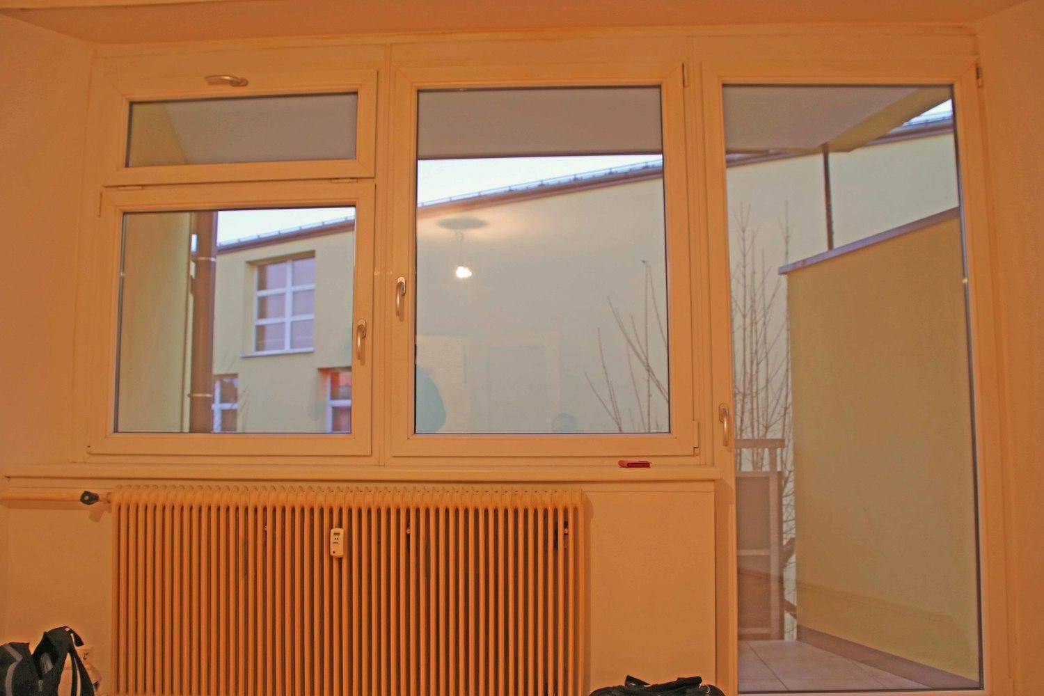 Fensterbereich mit Heizkörper und Blick auf den Innenhof sowie Zugang zum Balkon.