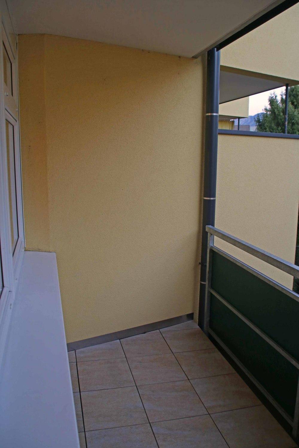 Kleiner gefliester Balkon mit gelber Wand und Metallgeländer.