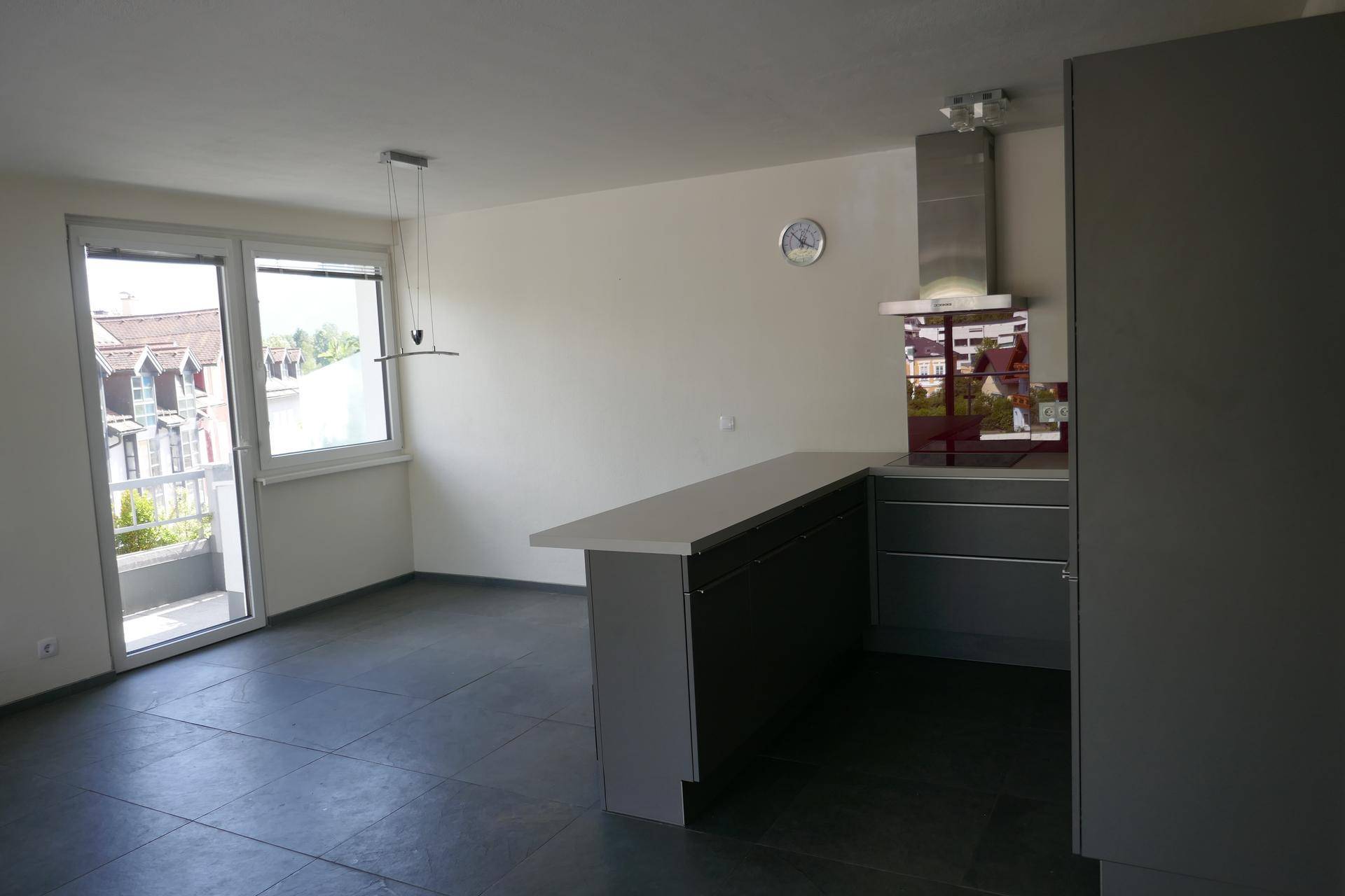 Moderne Küche mit grauen Schränken, Frühstücksbar und Zugang zu einem kleinen Balkon.