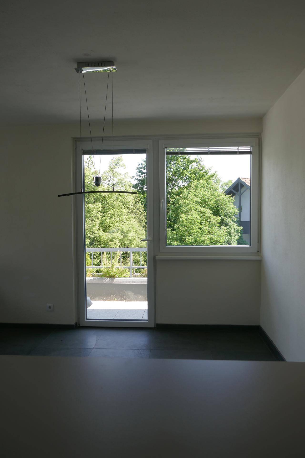 Heller Wohnbereich mit Zugang zum Balkon und Blick auf grüne Bäume, ausgestattet mit moderner Beleuchtung.