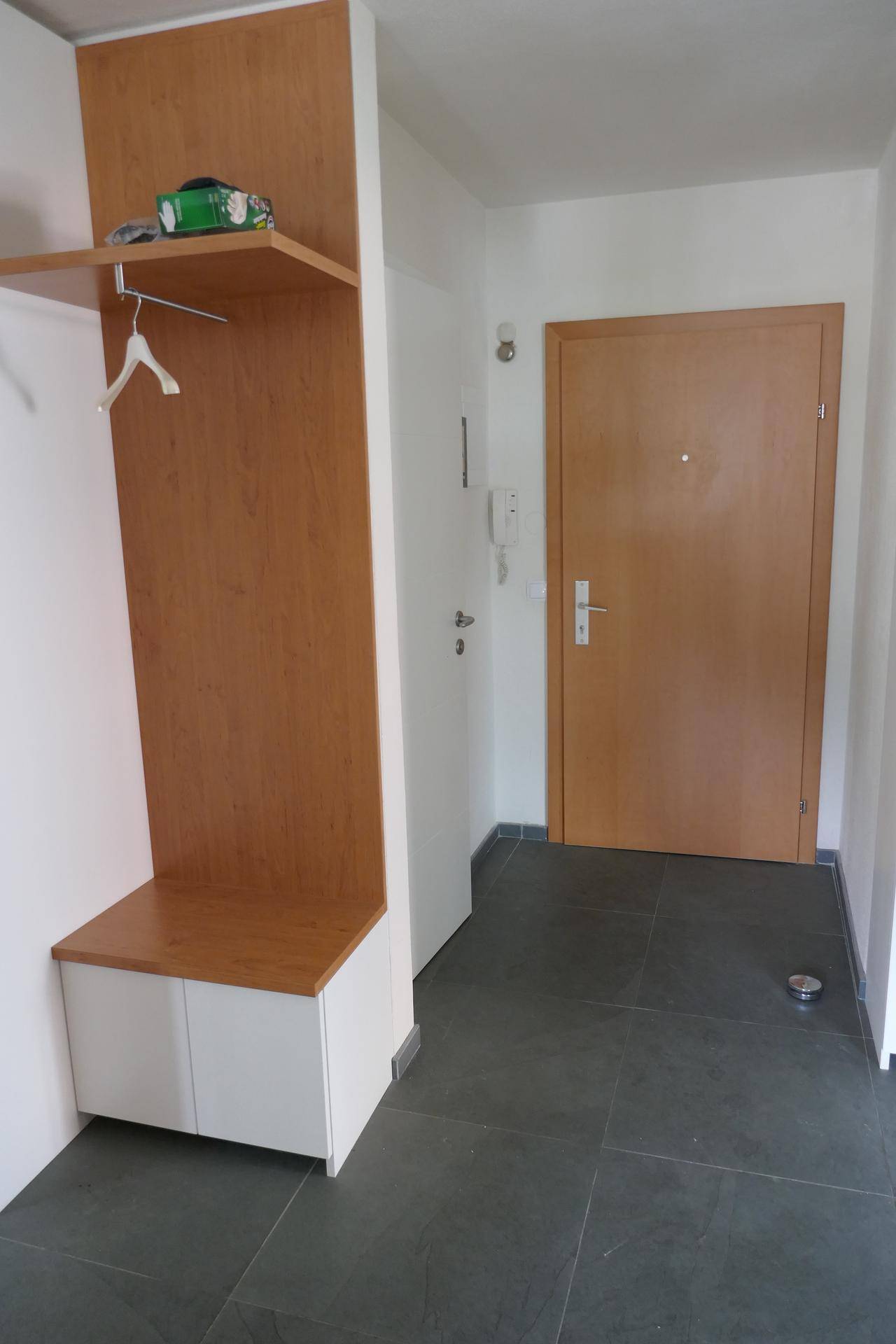 Eingangsbereich mit praktischer Garderobe aus hellem Holz und dunklem Fliesenboden.