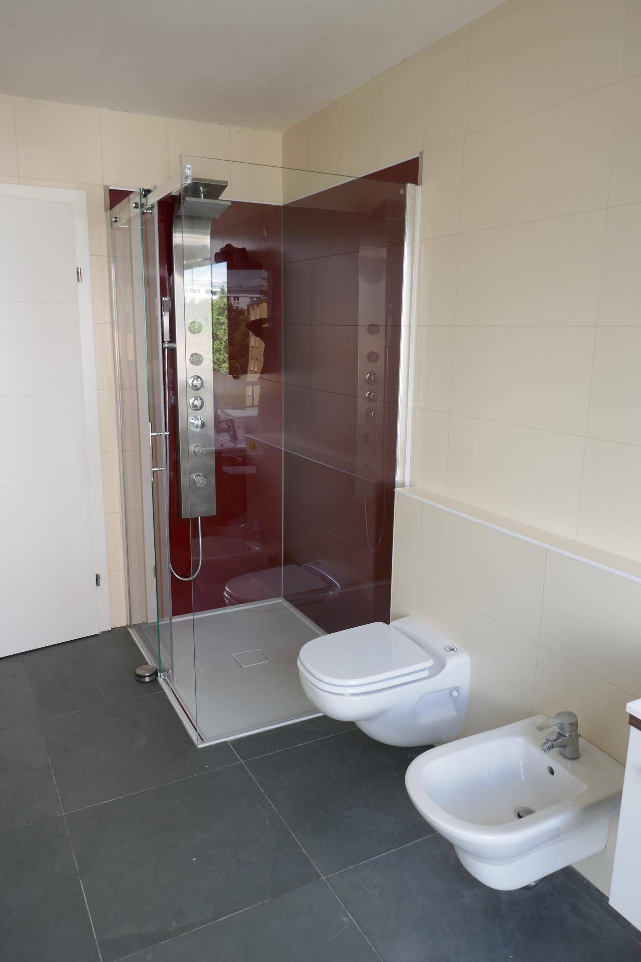 Geräumiges Badezimmer mit moderner Duschkabine, Bidet und Wand-WC, hell gefliest.