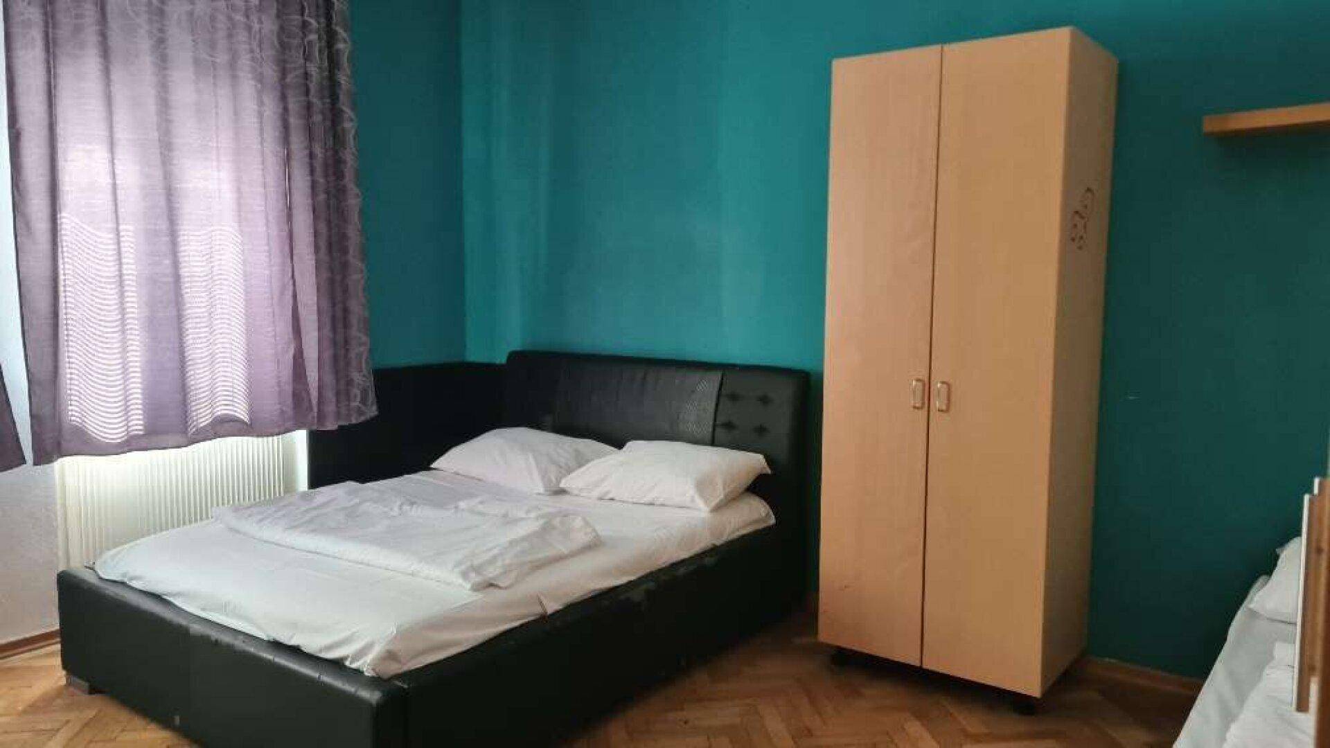 Schlafzimmer mit Einzelbett, Kleiderschrank und türkisfarbener Akzentwand.