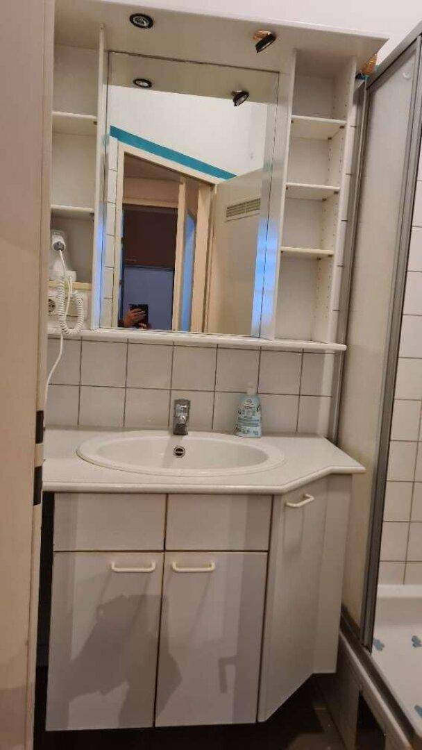 Einfaches Badezimmer mit Waschbecken, Spiegelschrank und weißen Wandfliesen.