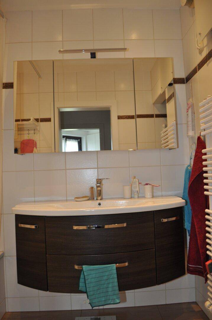 Badezimmer mit modernem Waschtisch, Spiegelschrank und Fliesen, ausgestattet mit einem Handtuchheizkörper.