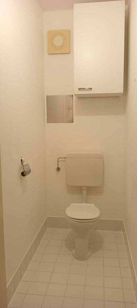Separates WC mit weißer Toilette und hellen Fliesen, funktional und sauber.