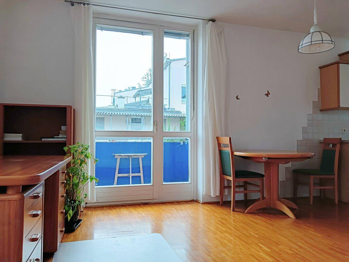 Heller Wohn- und Essbereich mit Holzboden und Zugang zu einem kleinen Balkon.