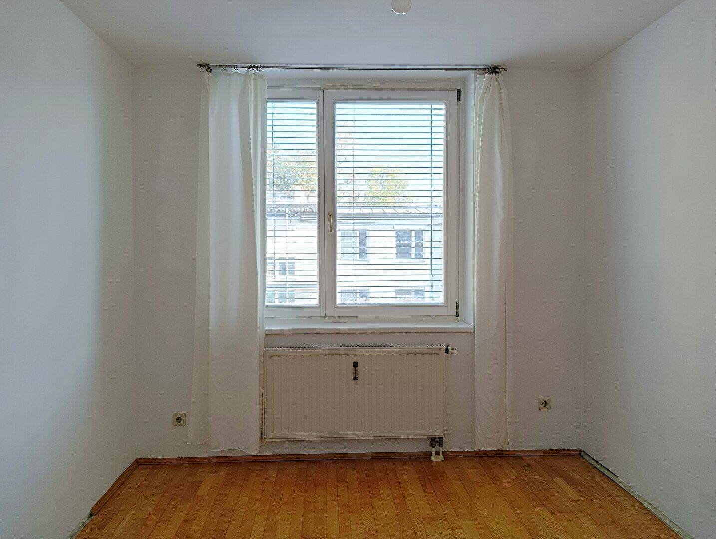 Leeres Zimmer mit Holzboden und großem Fenster, bereit zur individuellen Gestaltung.