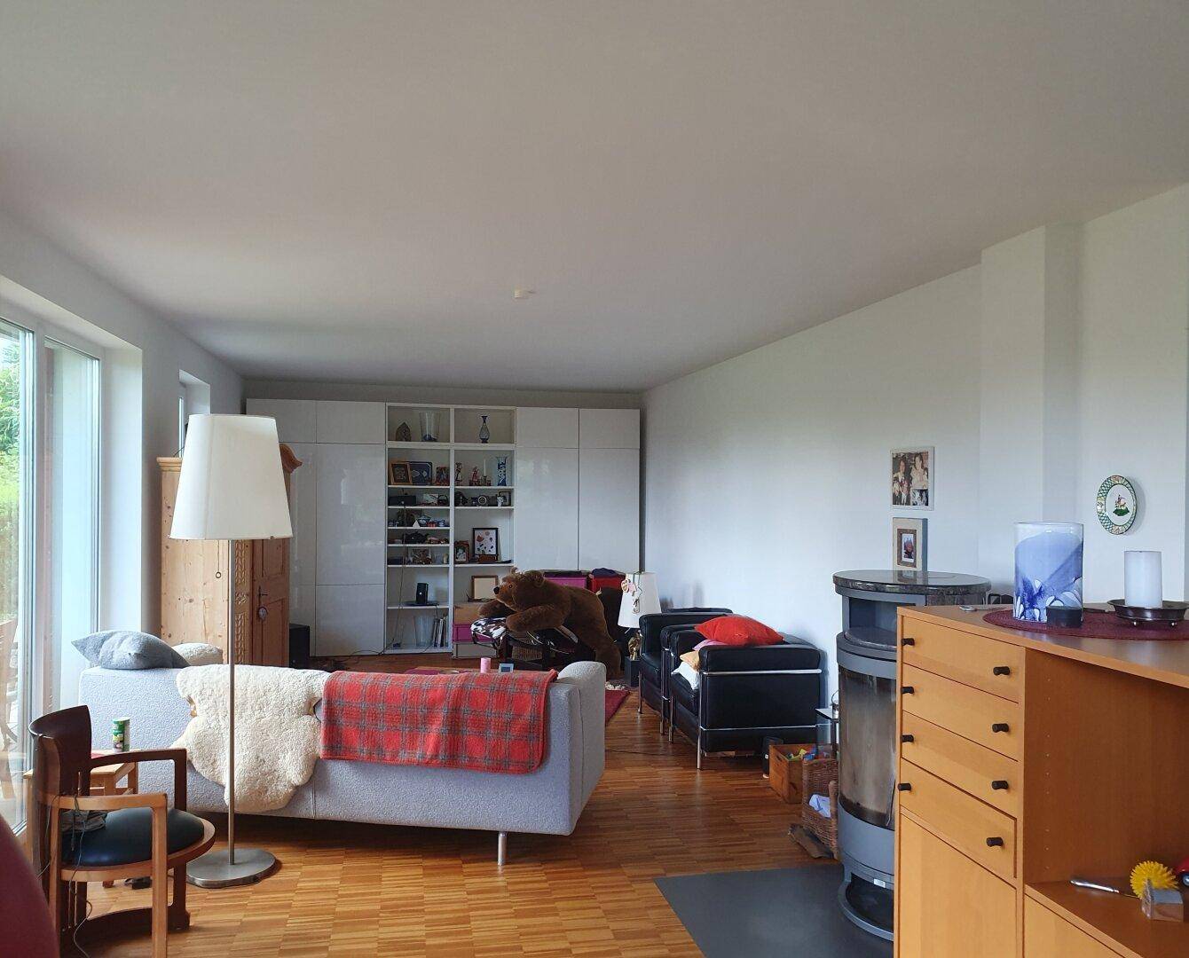 Geräumiges Wohnzimmer mit Holzboden, Kaminofen und großen Fenstern für viel Tageslicht.