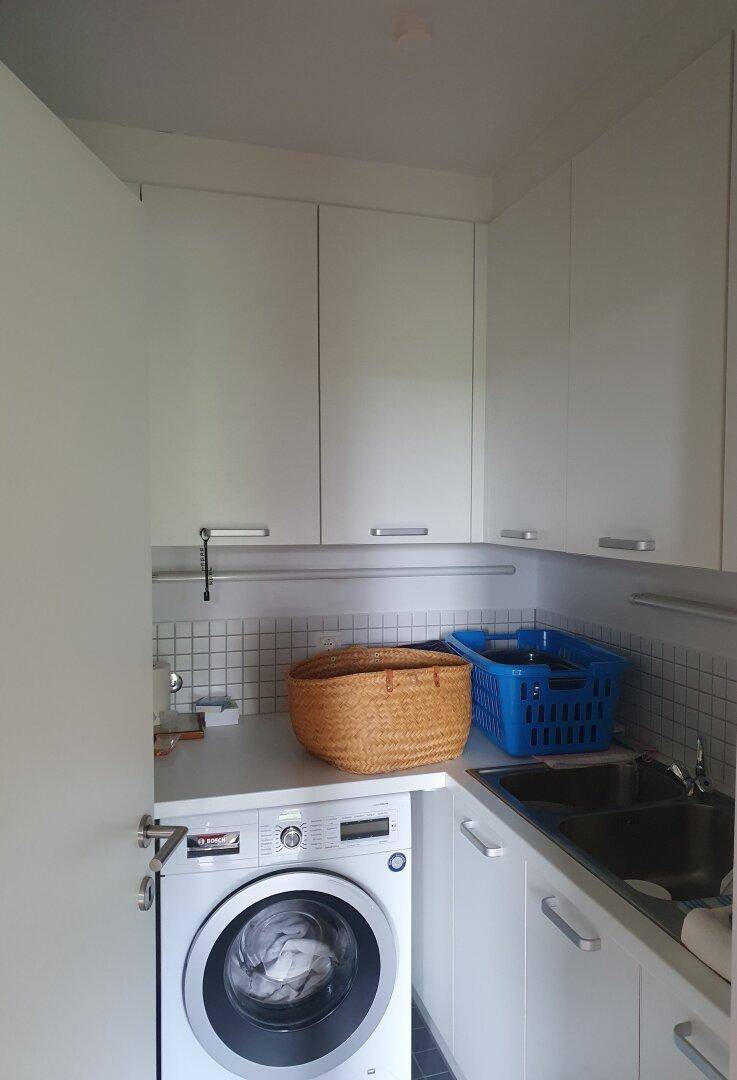 Praktischer Hauswirtschaftsraum mit Waschmaschine, Spülbecken und weißen Hängeschränken.