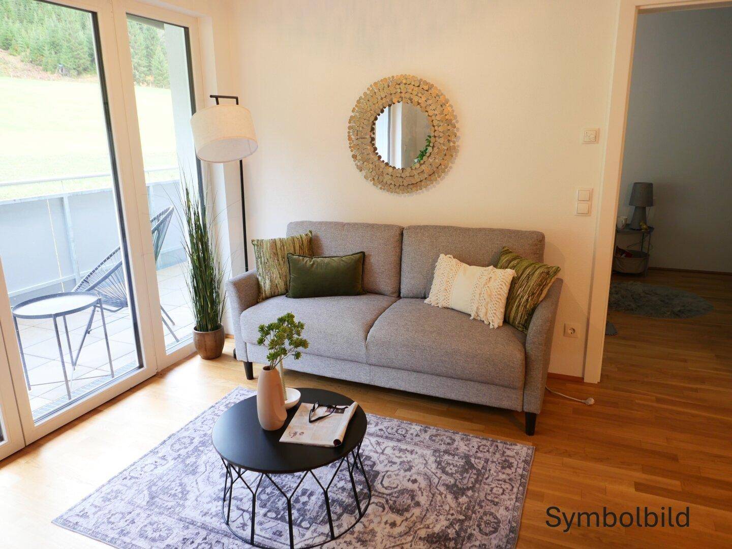 Gemütliches Wohnzimmer mit Sofa, Holzboden und Zugang zu einem Balkon mit Bergblick.