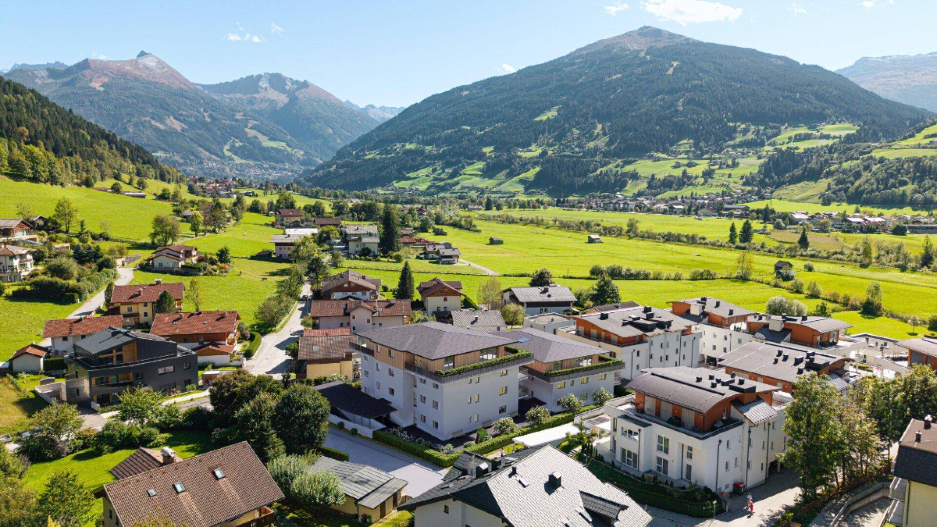 Luftaufnahme einer Siedlung in einem grünen Tal, umgeben von majestätischen Bergen und Natur.