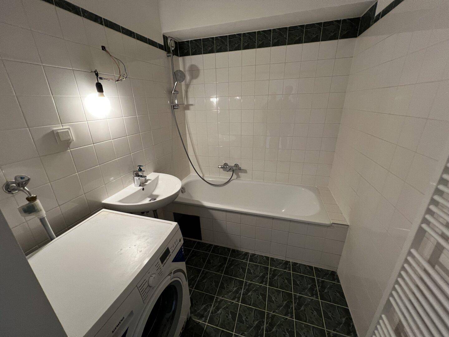 Gefliestes Badezimmer mit Badewanne, Dusche, Waschbecken und Platz für eine Waschmaschine.