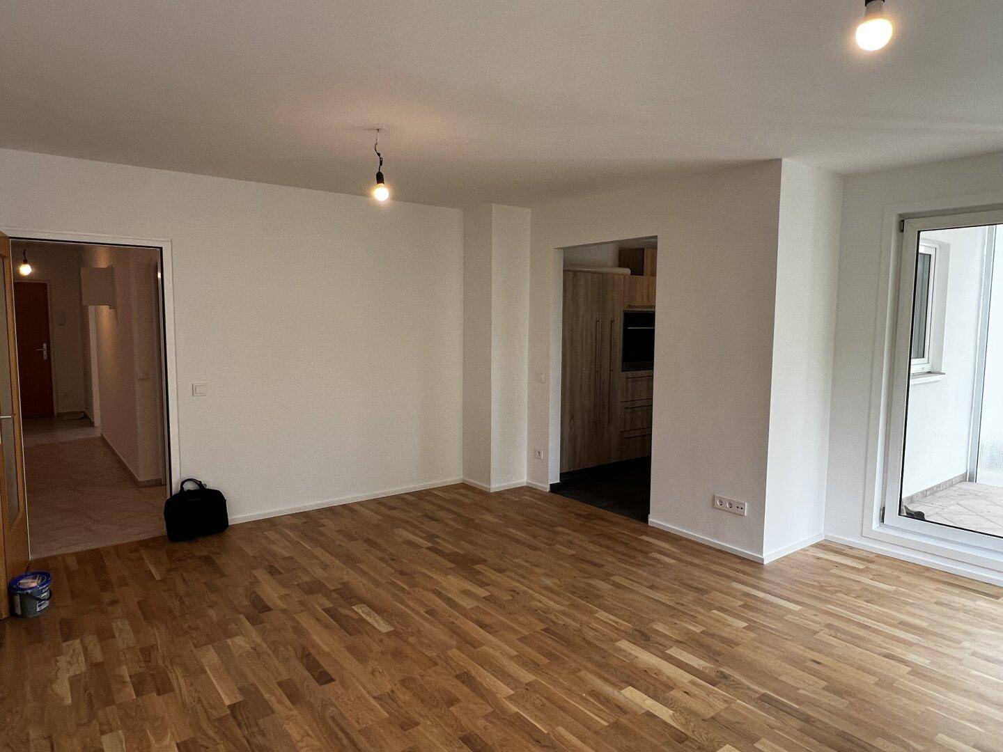 Heller Wohnbereich mit Parkettboden, Zugang zur Küche und einem Flur, frisch gestrichen.