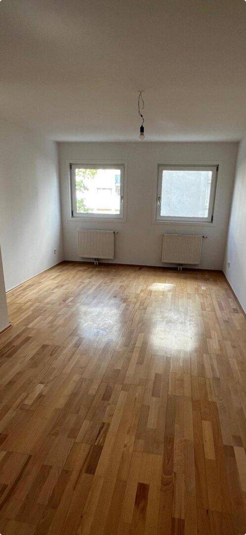 Geräumiges Zimmer mit Parkettboden und zwei Fenstern, die viel Tageslicht hereinlassen.