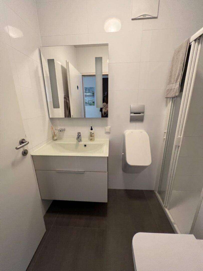 Modernes Badezimmer mit Waschtisch, Spiegel, Duschkabine und Wand-WC.