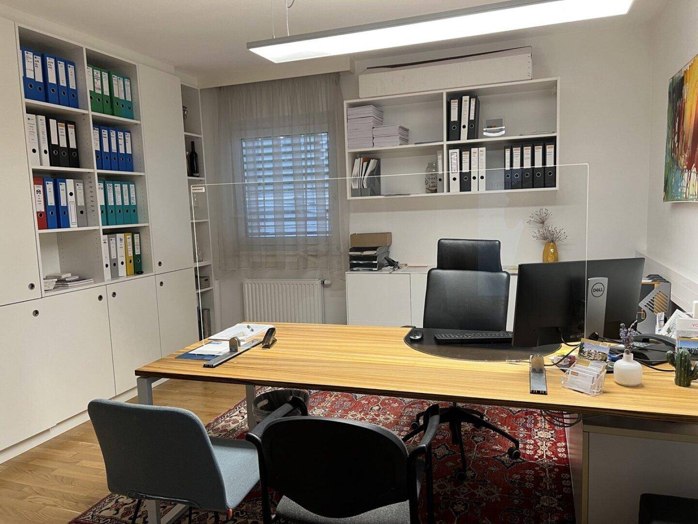 Helles Büro mit großem Schreibtisch, Bürostühlen und umfangreichen Aktenschränken.