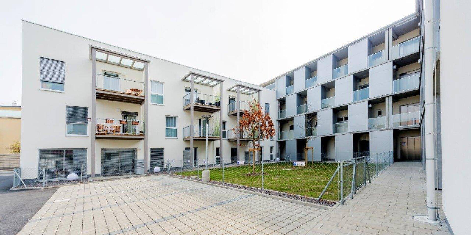 Modernes Mehrfamilienhaus mit Balkonen, gepflastertem Hof und Grünflächen.