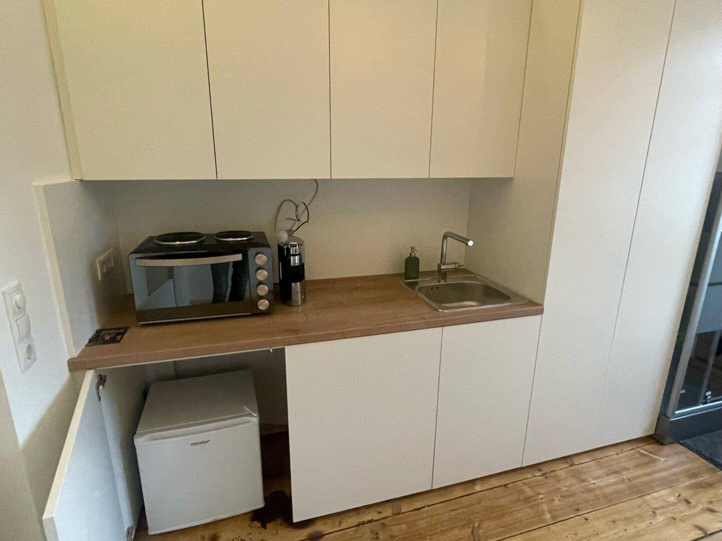 Kompakte Küchenzeile mit Spüle, Kochplatte, Toasterofen und integriertem Minikühlschrank.